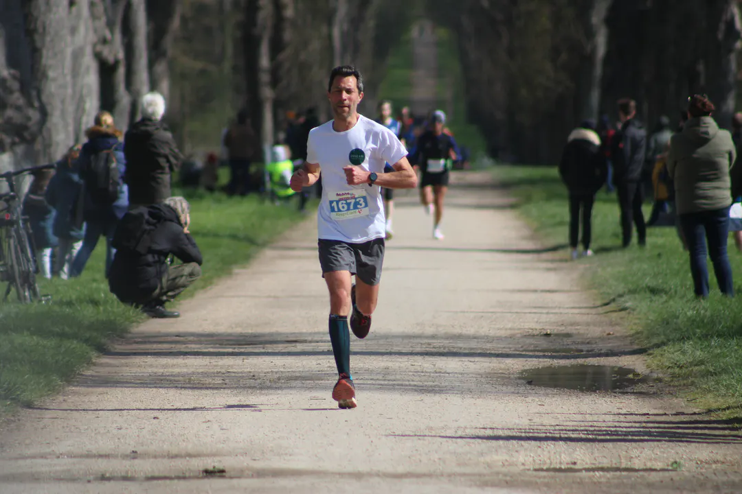 Coureur d'un semi-marathon sur une allée de parc en forêt, dossard 1673 bien lisible sur la poitrine, spectateurs sur les bas-côtés