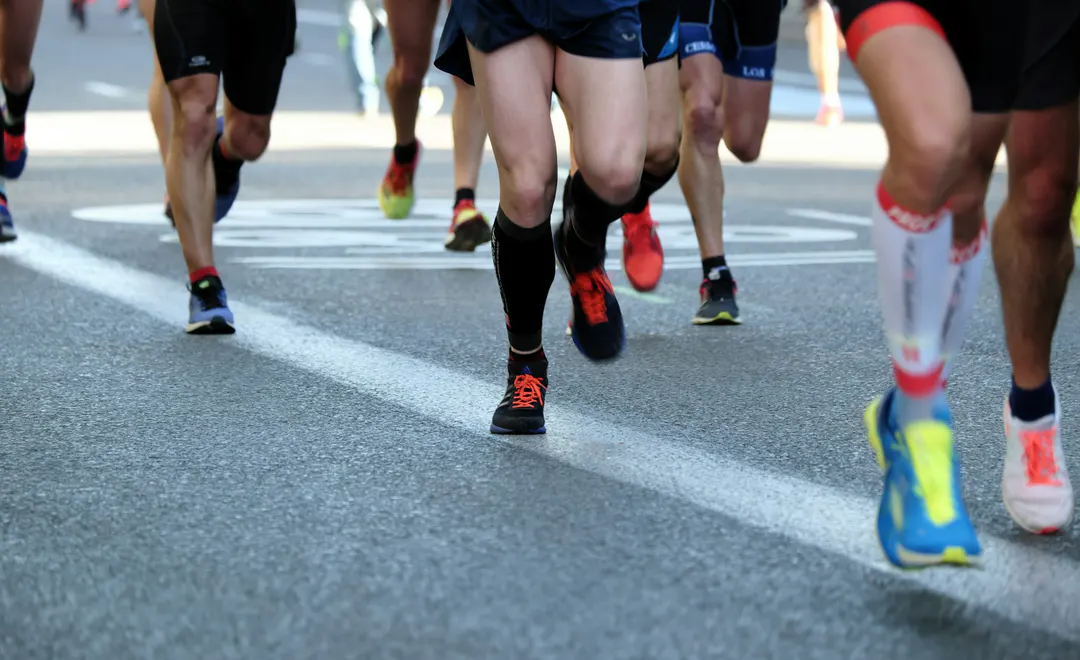 Jambes de coureurs en pleine foulée sur une route goudronnée pendant une course, sans aucun visage visible